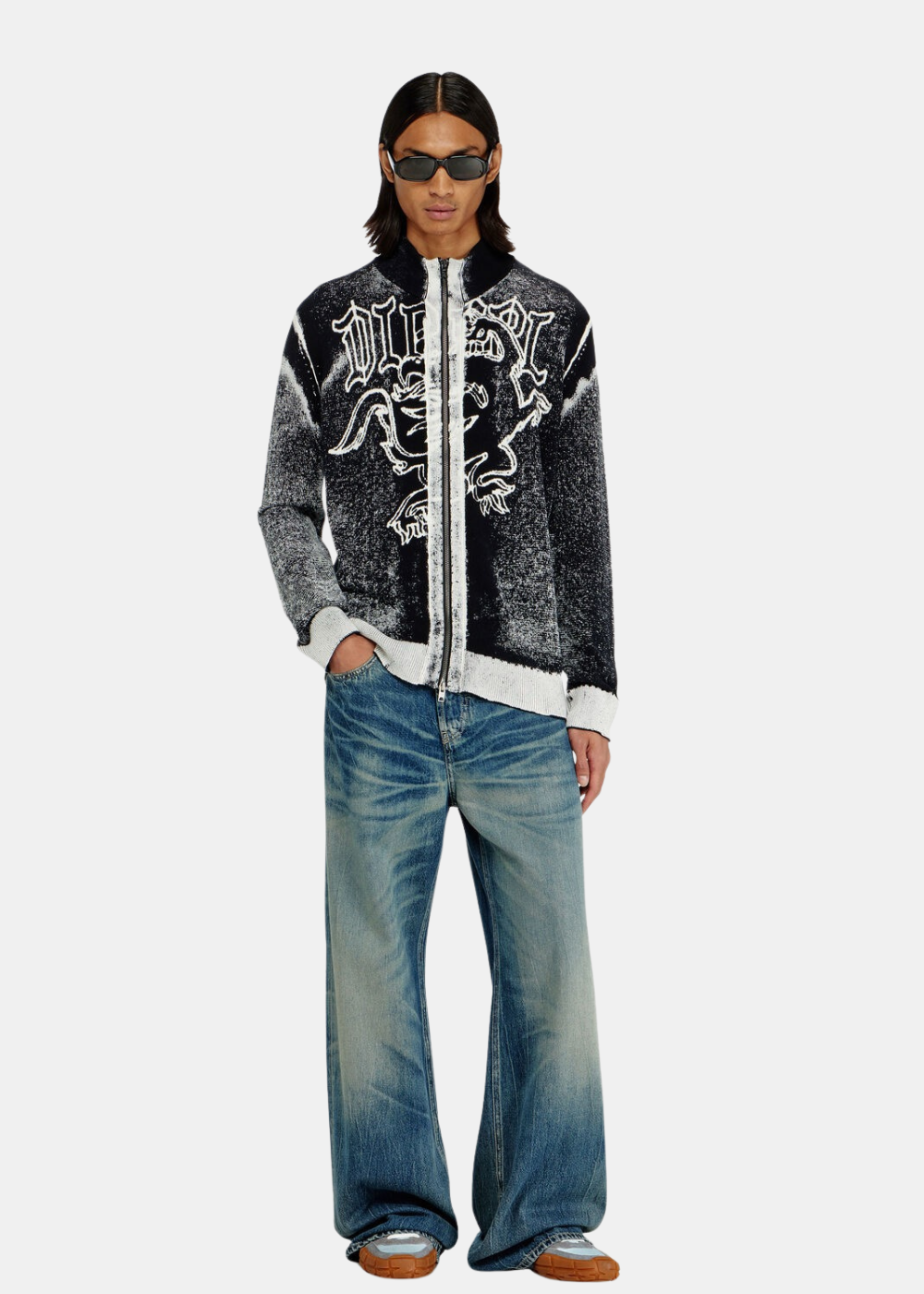 Silhouette complète du mannequin portant le cardigan zippé Diesel, un jean large délavé et des lunettes de soleil.