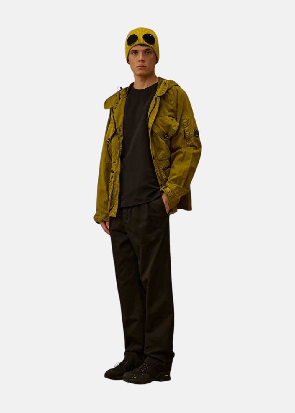 Silhouette complète avec parka jaune moutarde, t-shirt noir, pantalon cargo et bonnet jaune à lunettes.