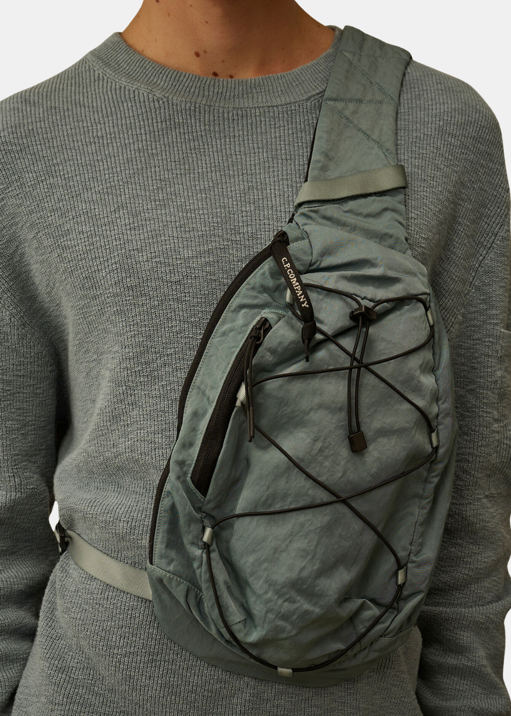 Gros plan sur le sac crossbody C.P. Company en nylon bleu montrant la fermeture zippée et les détails techniques.