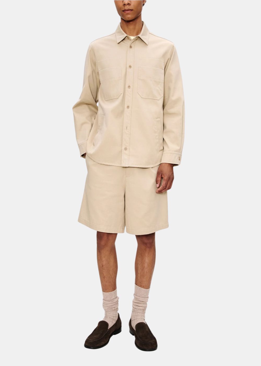 Look complet de face avec une surchemise beige A.P.C. portée avec un short assorti et des mocassins marron.