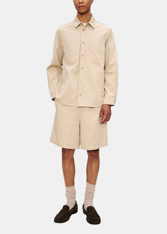Look complet de face avec une surchemise beige A.P.C. portée avec un short assorti et des mocassins marron.
