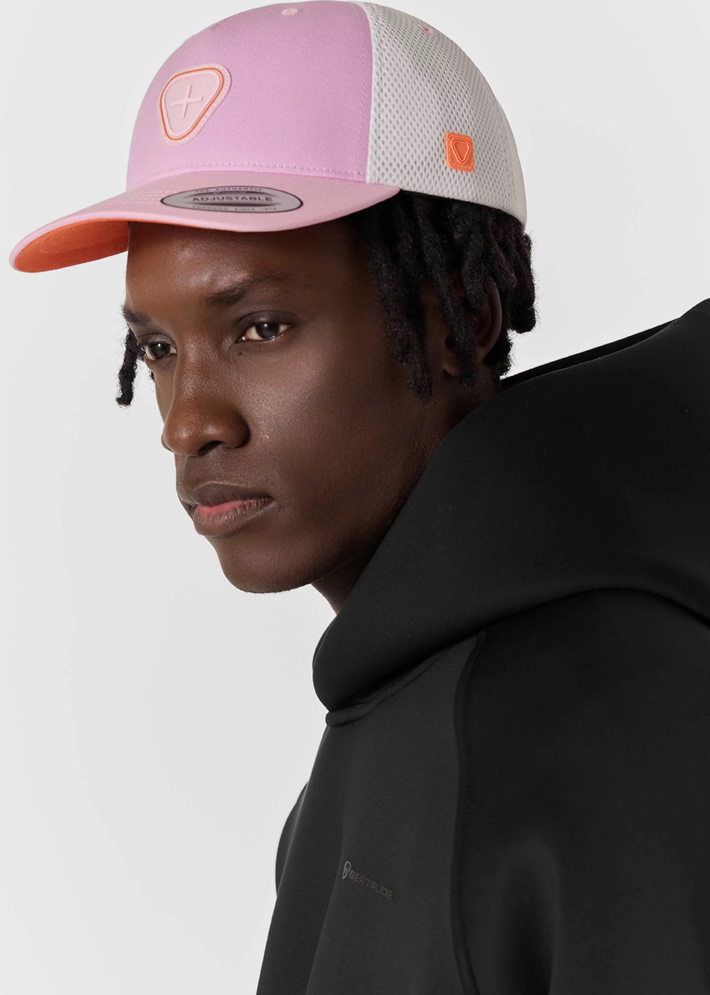Mannequin homme de profil portant la casquette trucker Gertrude rose et blanche avec un sweat à capuche noir