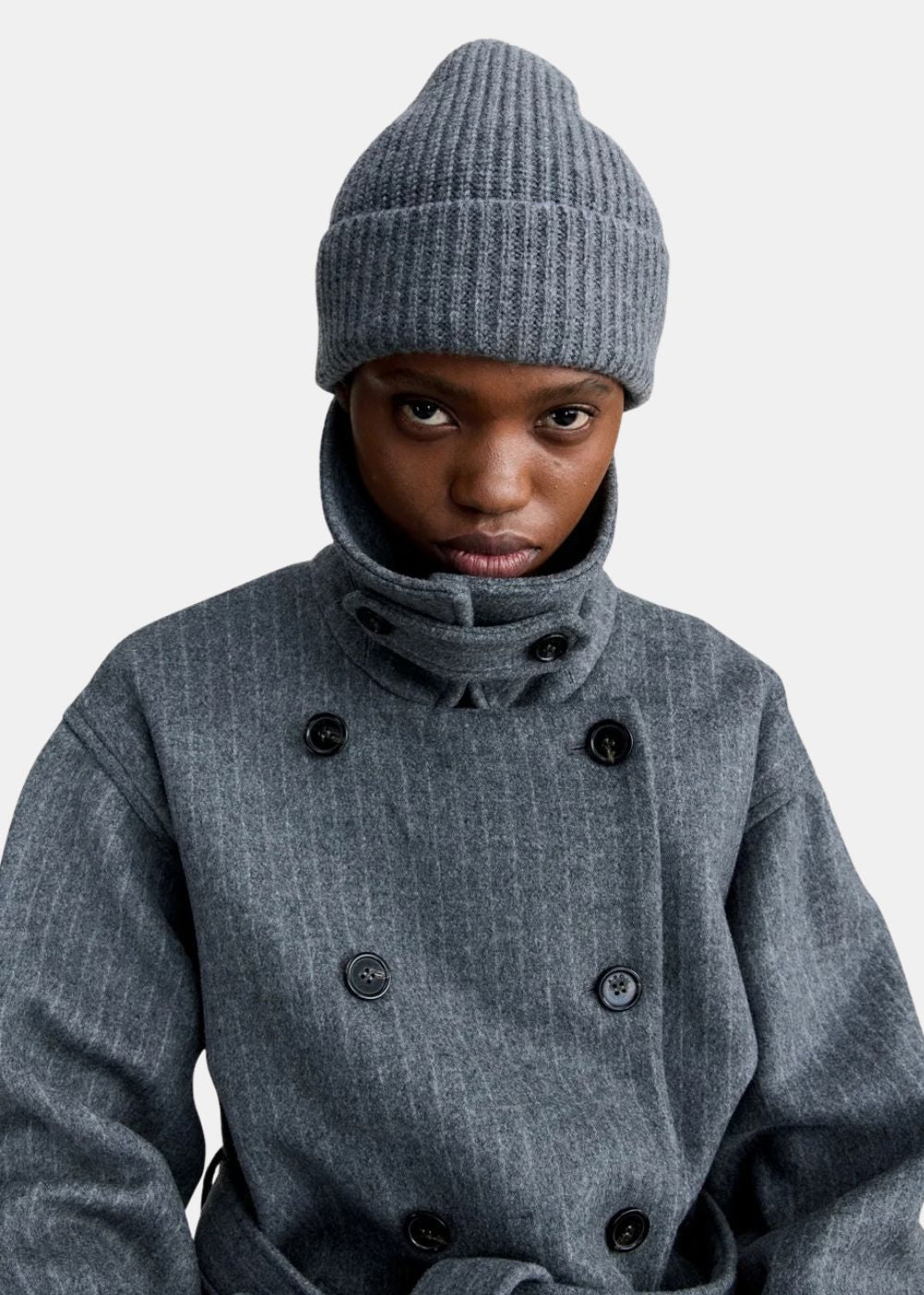 Mannequin portant le bonnet en maille côtelée gris A.P.C. associé à un caban gris.