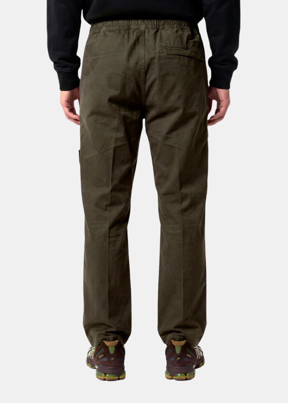 Modèle portant le pantalon Stone Island vu de dos. Révèle la ceinture élastique confortable, la poche arrière passepoilée et le plissé naturel du tissu en Ripstop résistant.