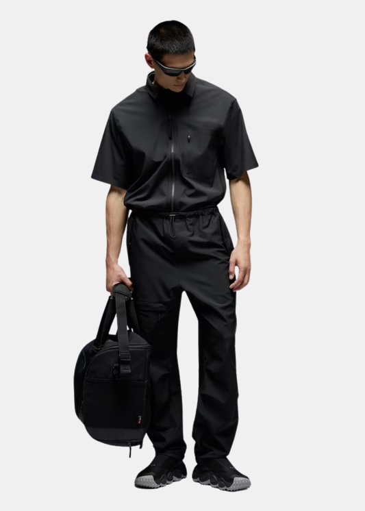 Homme portant le pantalon noir Oakley avec chemise zippée assortie et sac de sport noir.