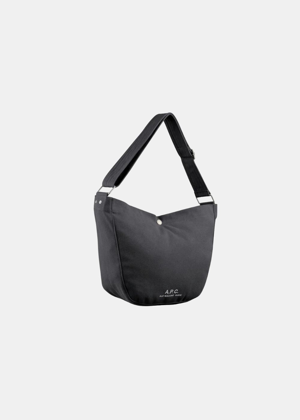 Vue de trois-quarts montrant le volume et la profondeur du sac besace A.P.C. noir. On aperçoit la largeur de la base, le tombé souple de la toile et les détails des rivets métalliques sur la bandoulière.
