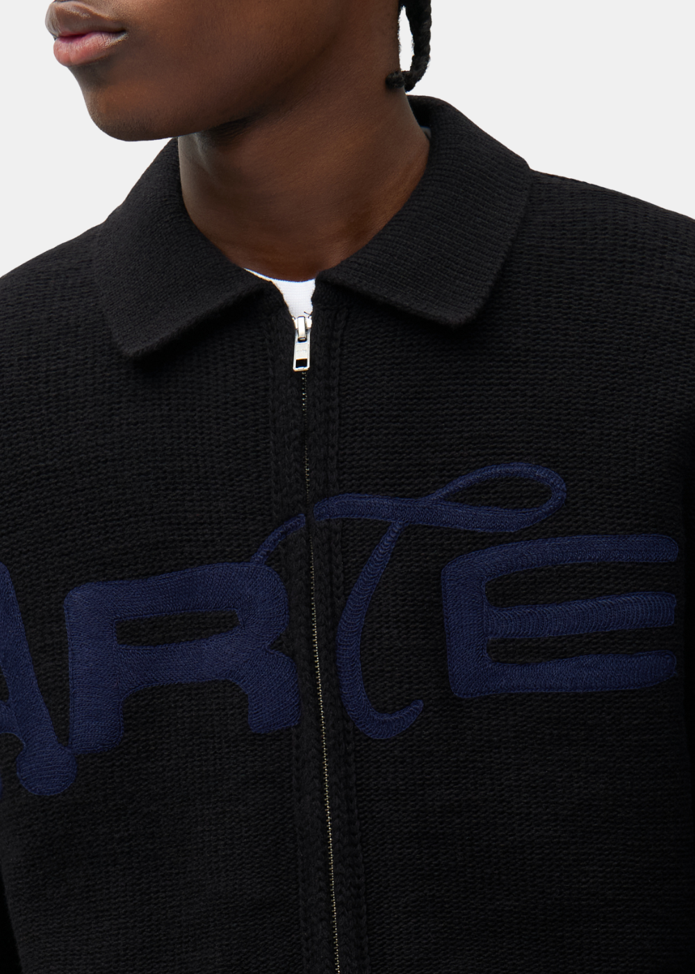 Gros plan sur le col, le zip métallique et le logo ARTE bleu brodé sur le cardigan noir Arte-Antwerp.