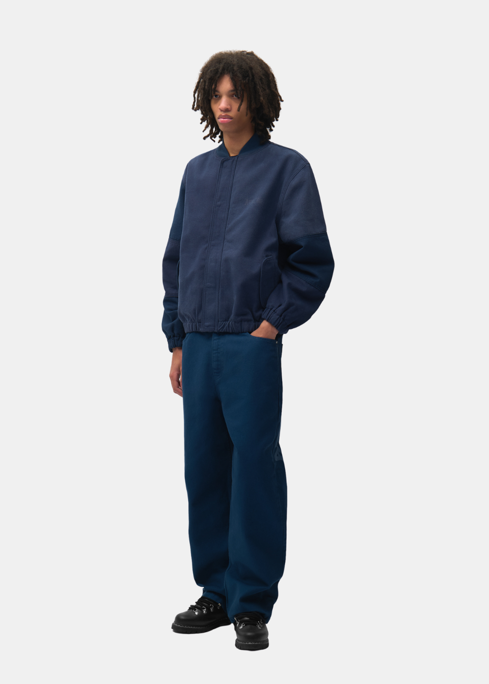 Mannequin à cheveux bouclés portant le pantalon droit marine Arte-Antwerp avec une veste assortie et des chaussures noires.