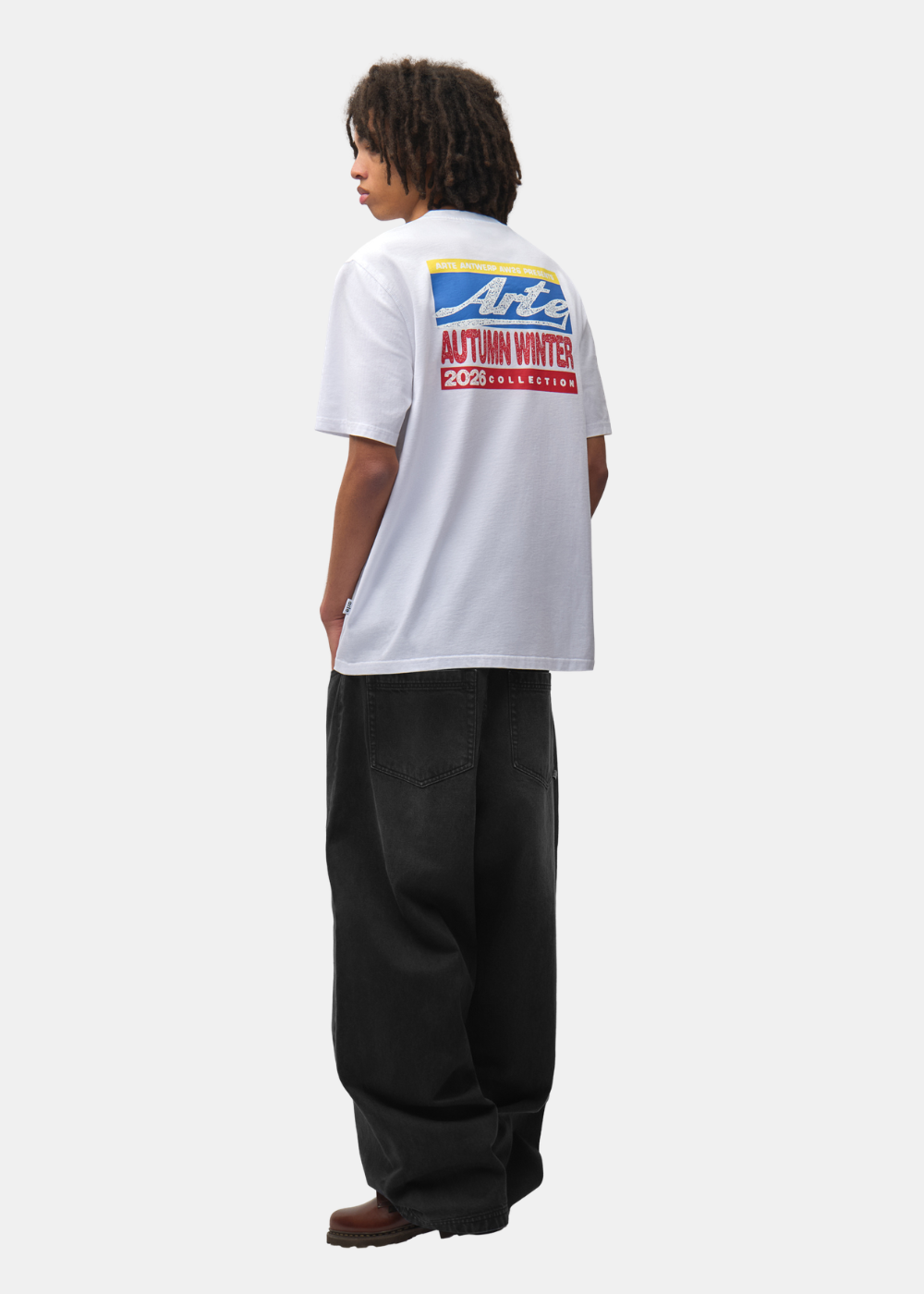 Mannequin portant le t-shirt blanc Arte-Antwerp avec graphique au dos, pantalon large noir et baskets, de dos.