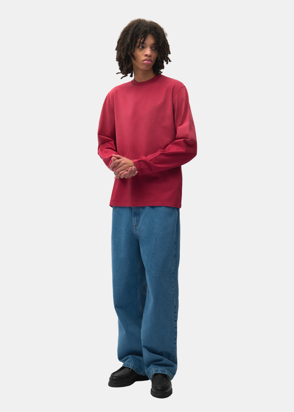 Mannequin de face portant le t-shirt manches longues bordeaux Arte-Antwerp, un jean bleu ample et des chaussures noires.