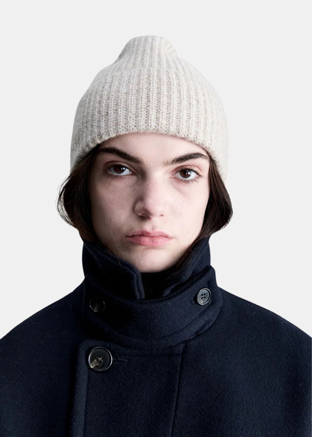 Mannequin portant le bonnet en maille côtelée beige A.P.C. associé à un caban bleu marine.