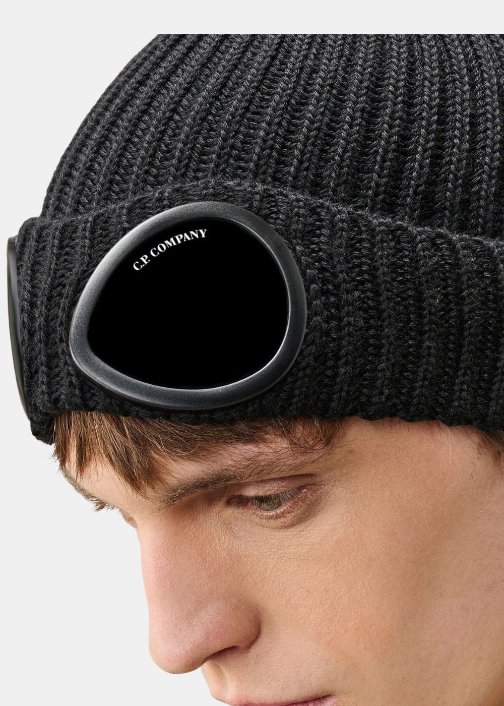 Gros plan sur le verre de lunette signature C.P. Company fixé sur le revers du bonnet en laine noir