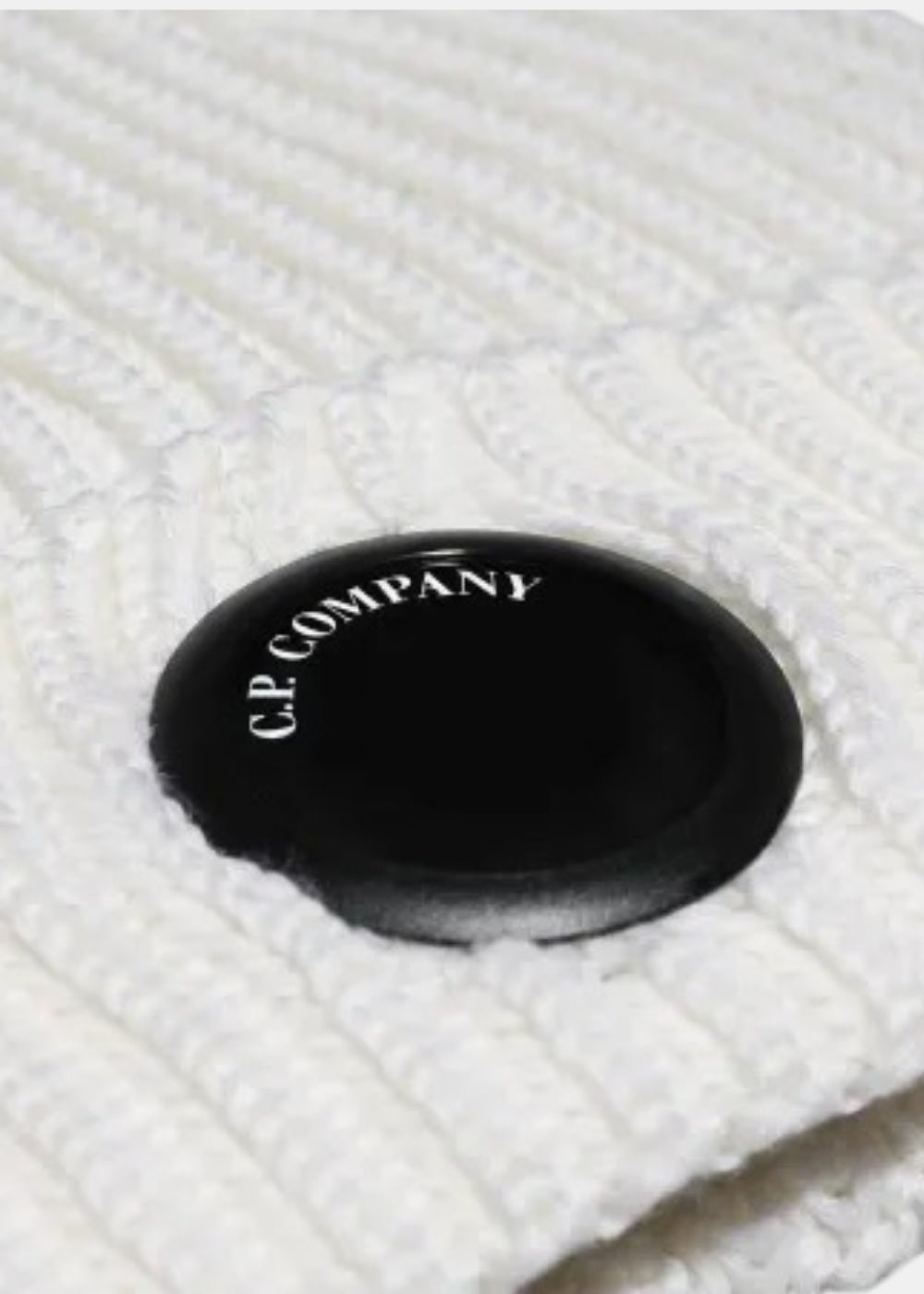 Packshot de face d'un bonnet blanc en maille côtelée C.P. Company à bord retroussé orné de la Lens noire mate.