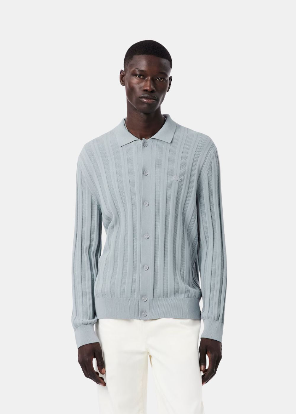 Mannequin portant le cardigan col polo bleu gris Lacoste boutonné avec un pantalon blanc.