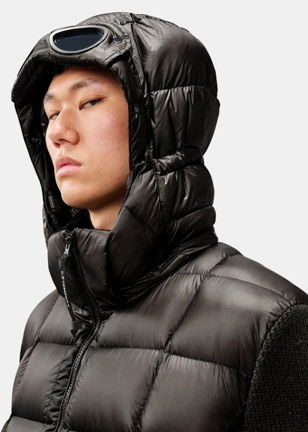 Gros plan porté sur la capuche matelassée Goggle C.P. Company noire avec verre de lunette relevé
