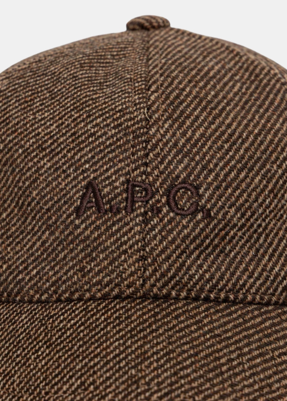 Gros plan sur le logo A.P.C. brodé ton sur ton et le tissu chiné d'une casquette baseball marron.