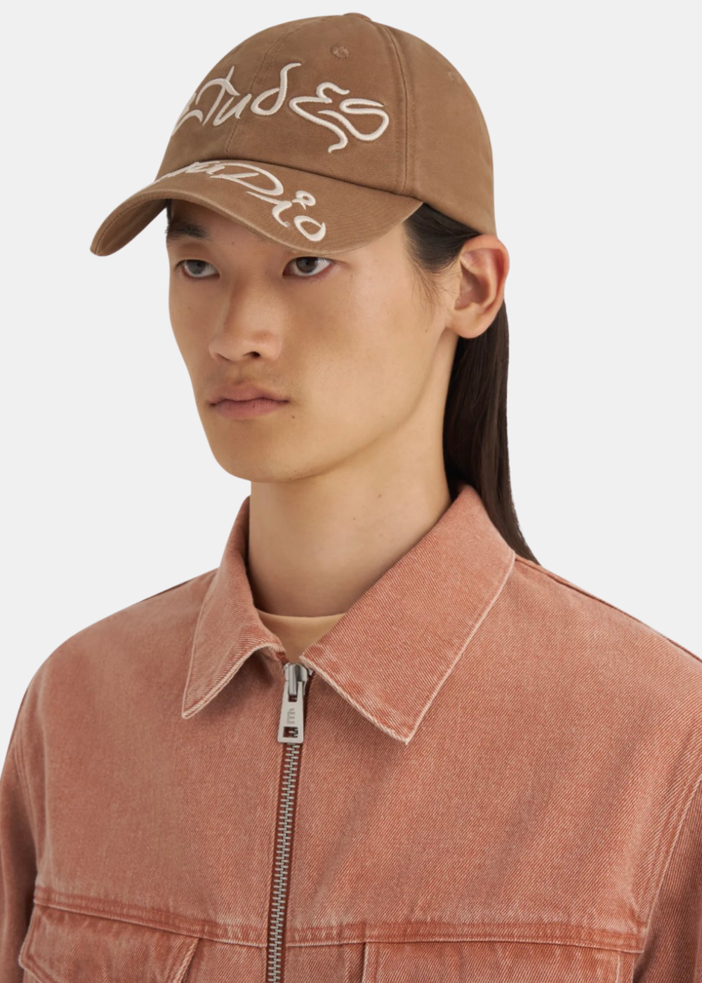 Homme de face portant la casquette camel Études Studio avec une chemise blanche à rayures bleues
