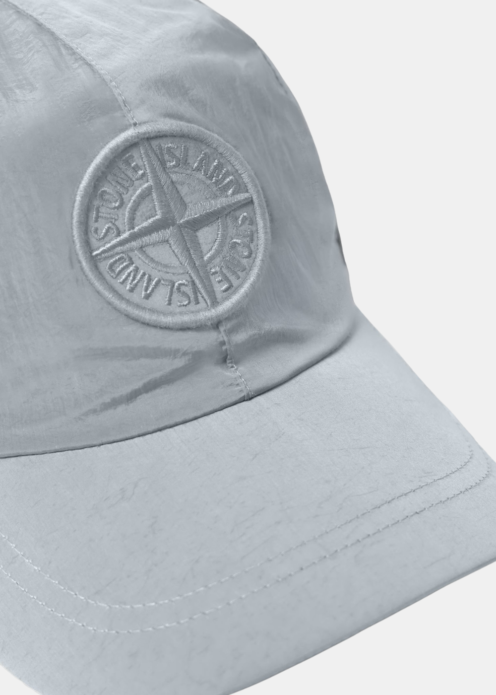 Gros plan sur le patch boussole brodé ton sur ton et la texture froissée de la casquette grise Stone Island.
