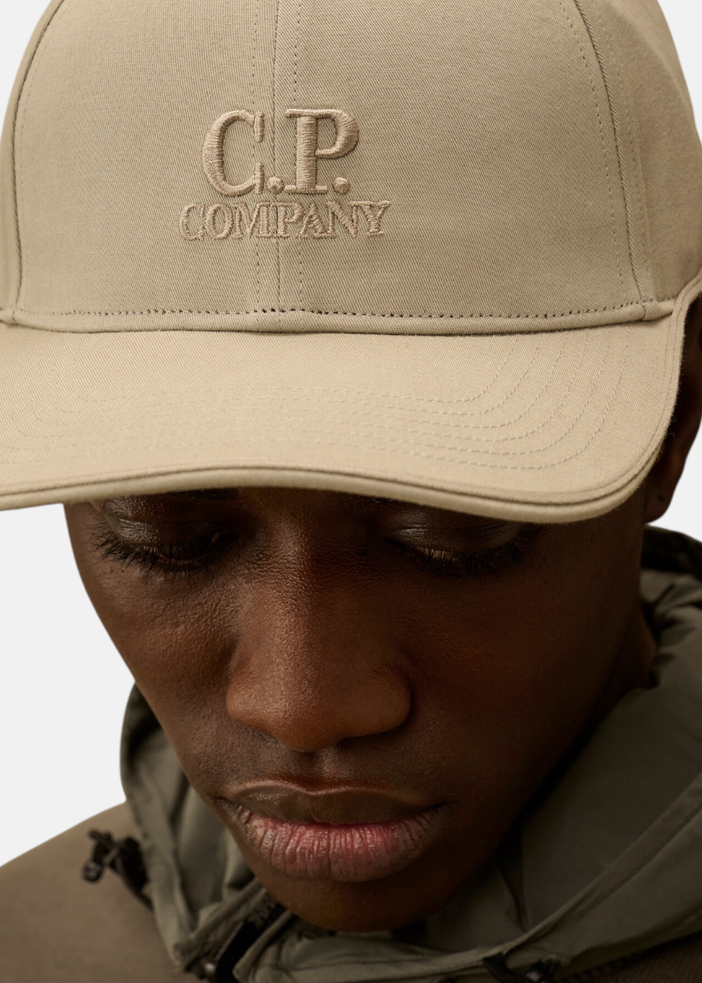 Gros plan sur la partie avant de la casquette beige C.P. Company montrant le logo brodé en relief ton sur ton