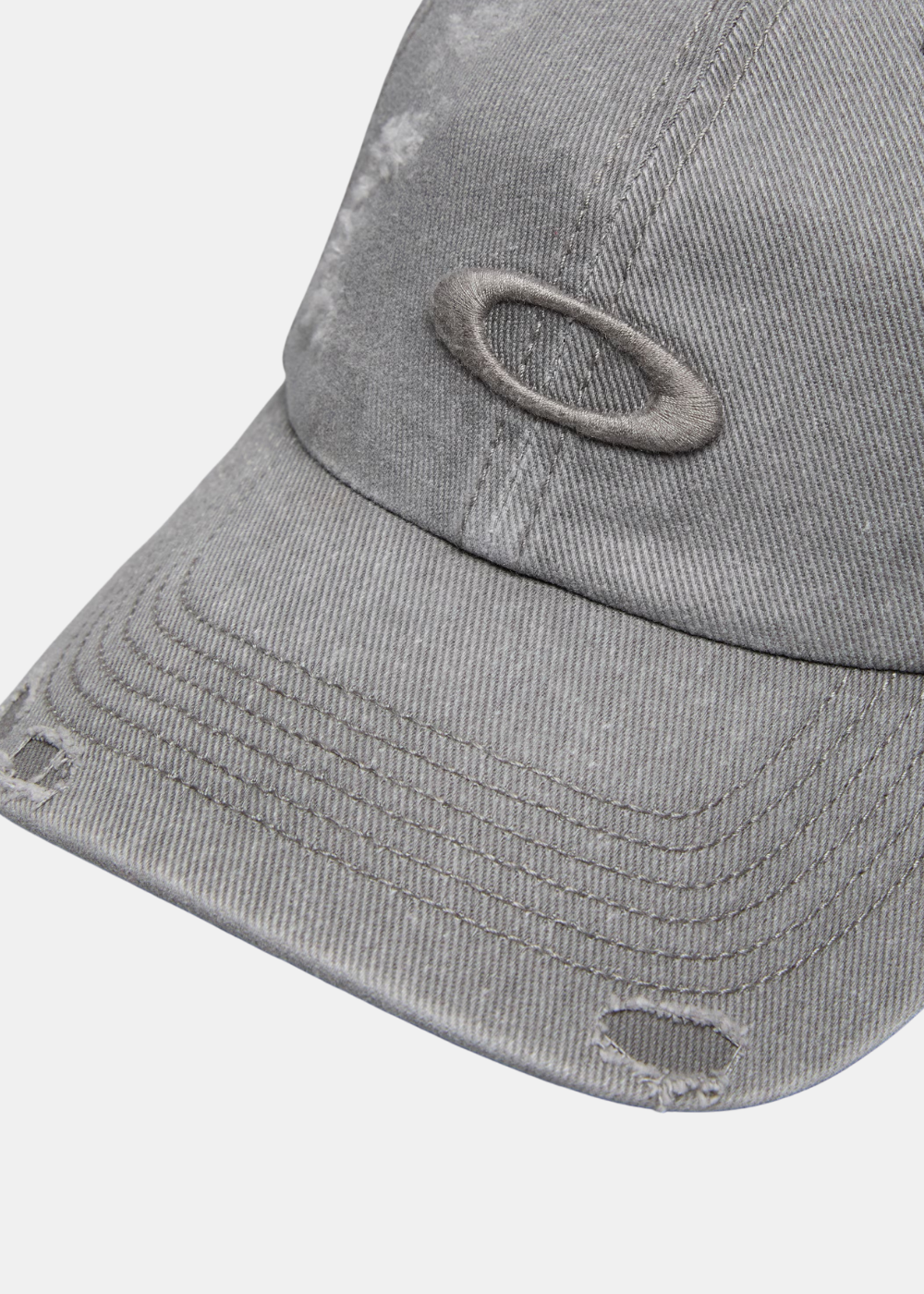 Gros plan sur le logo Ellipse Oakley brodé ton sur ton et la finition usée effet usé sur la visière d'une casquette grise