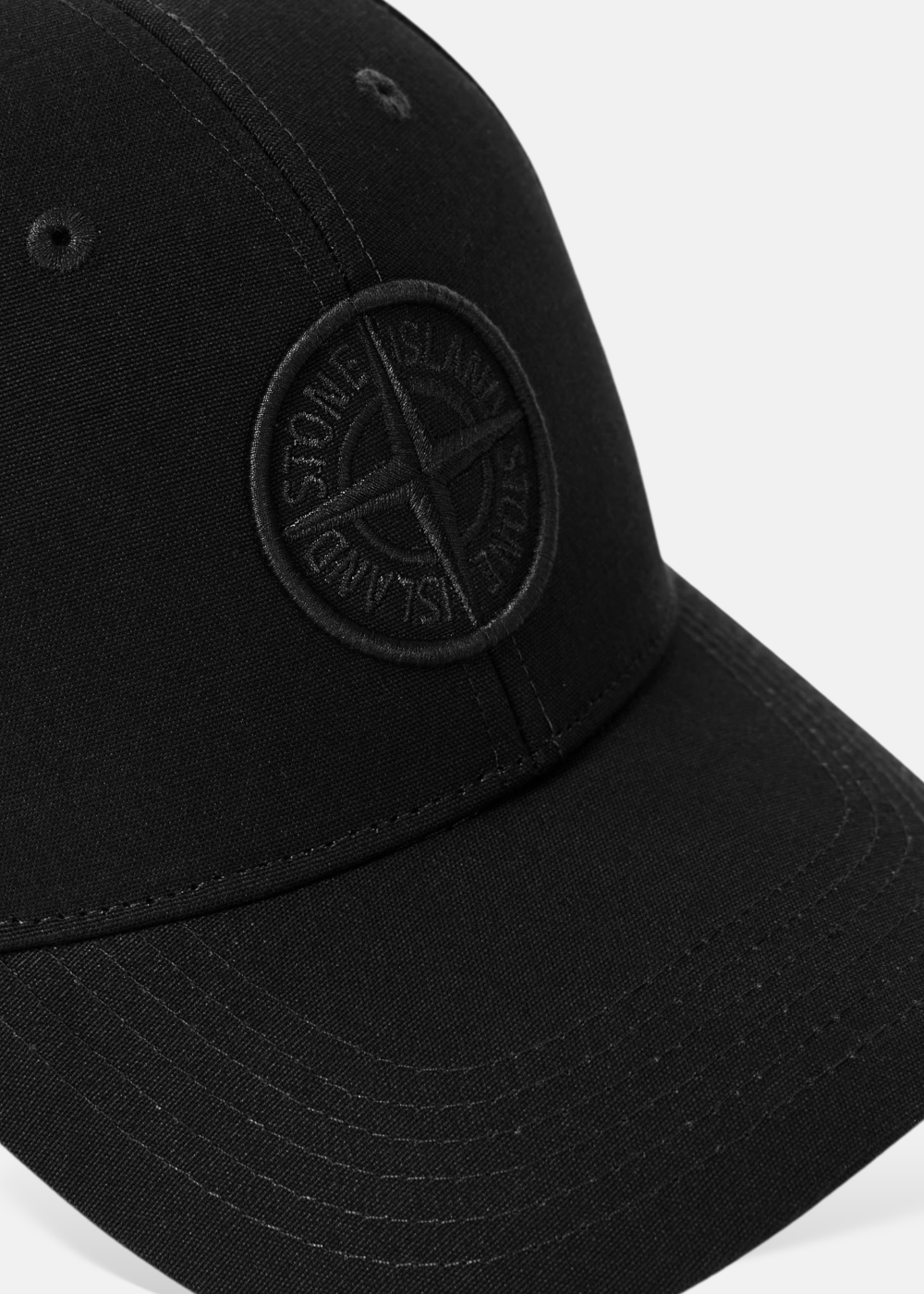 Gros plan sur le logo Stone Island brodé ton sur ton sur la casquette noire.