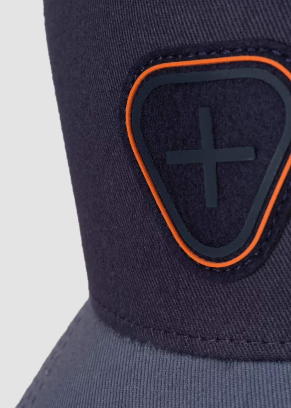 Gros plan sur le patch écusson brodé signe Gertrude de couleur bleu marine avec liseré orange sur la calotte