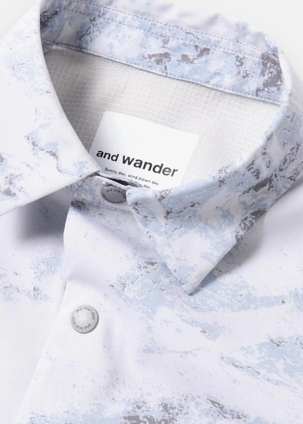 Gros plan sur le col et l'étiquette logo And Wander de la chemise technique imprimée.
