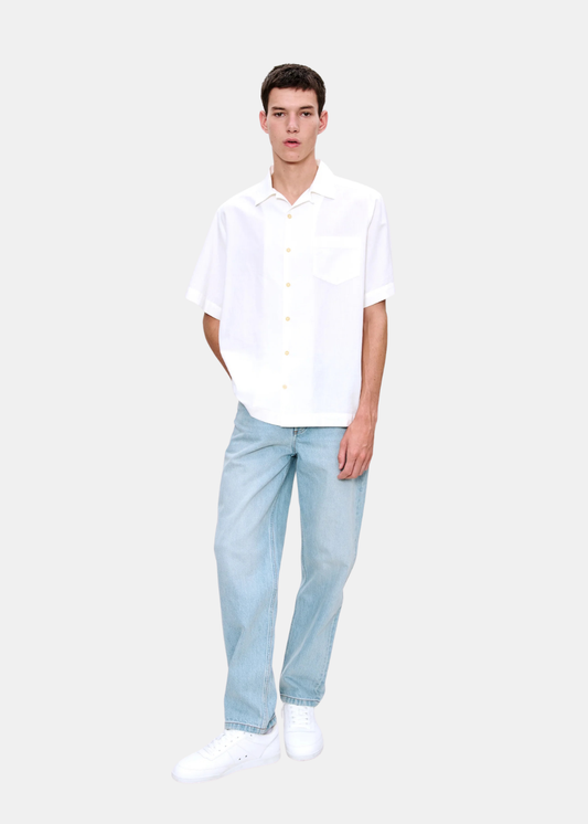 Silhouette complète d'un homme portant la chemise A.P.C. Jude blanche avec un jean clair et des baskets blanches.