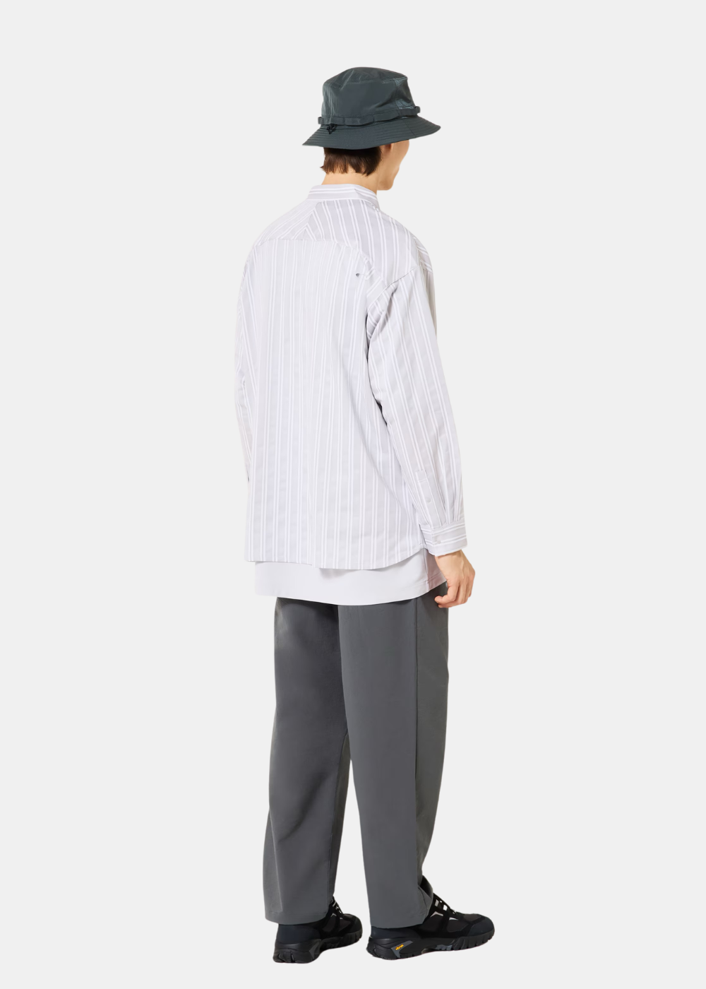 Mannequin de dos portant la chemise Oakley blanche à rayures verticales et un pantalon noir avec sac à dos.