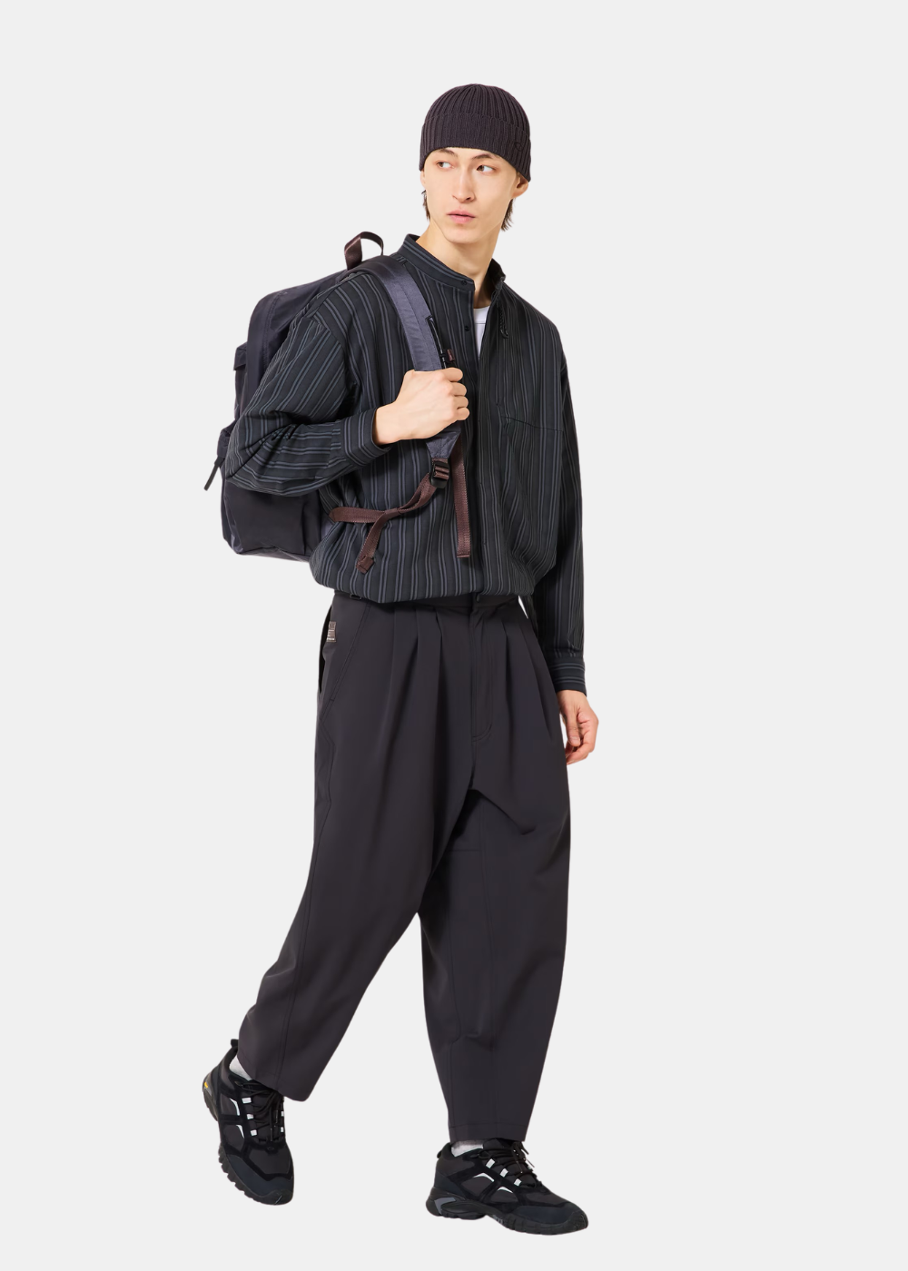 Mannequin portant la chemise Oakley grise à rayures, un pantalon noir, un bonnet et un sac à dos, de face.