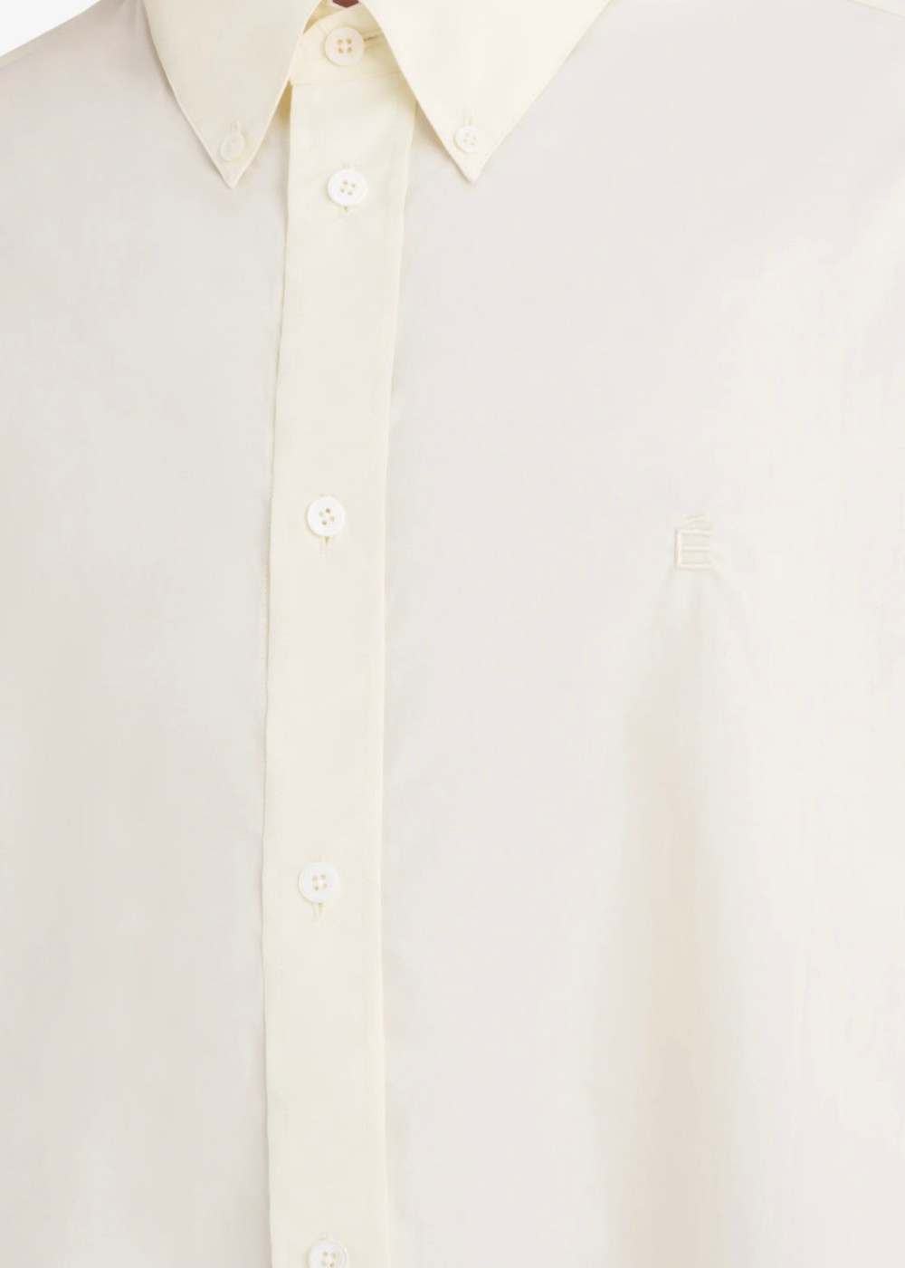Gros plan sur la poitrine d'une chemise blanc cassé montrant le logo É brodé et la texture fine des rayures