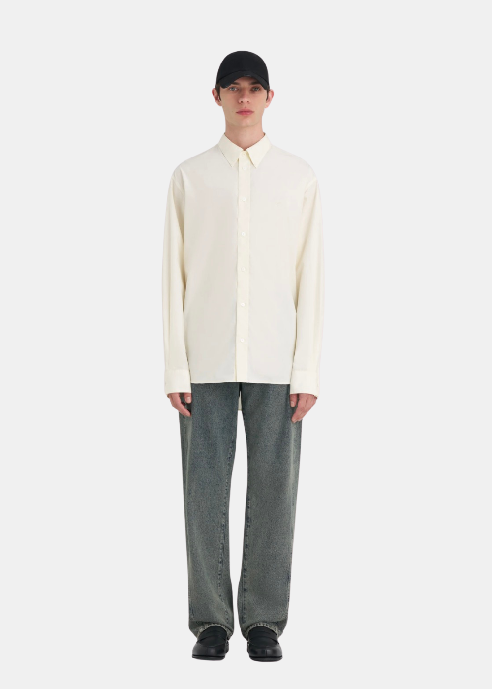 Vue en pied d'un homme portant la chemise Études Studio blanc cassé, un jean large gris et des chaussures noires