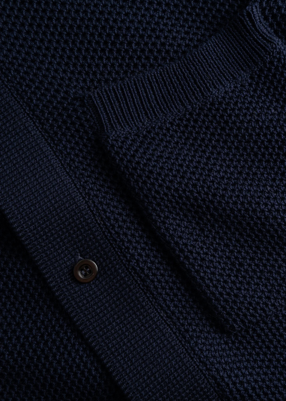 Détail de la maille texturée marine et d'un bouton brun de la chemise Homme Norse Projects.