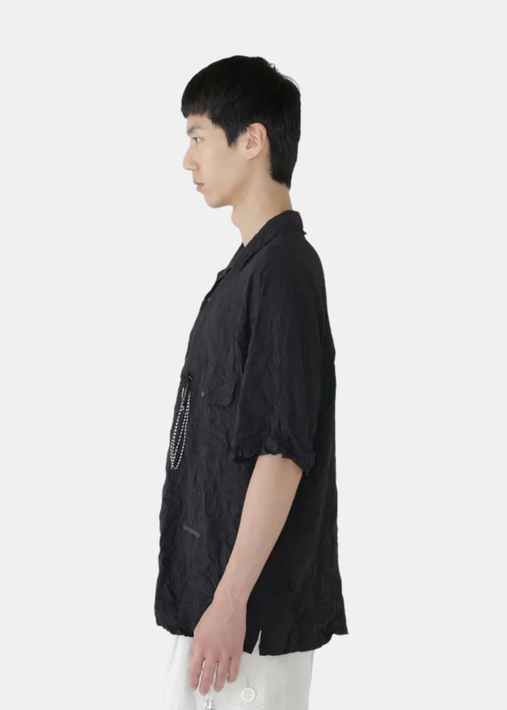 Chemise à manches courtes noire And Wander en tissu plissé, portée de profil par un mannequin.