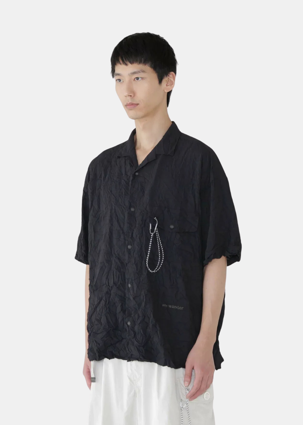 Chemise plissée noire And Wander avec mousqueton sur la poche poitrine, portée de trois-quarts.