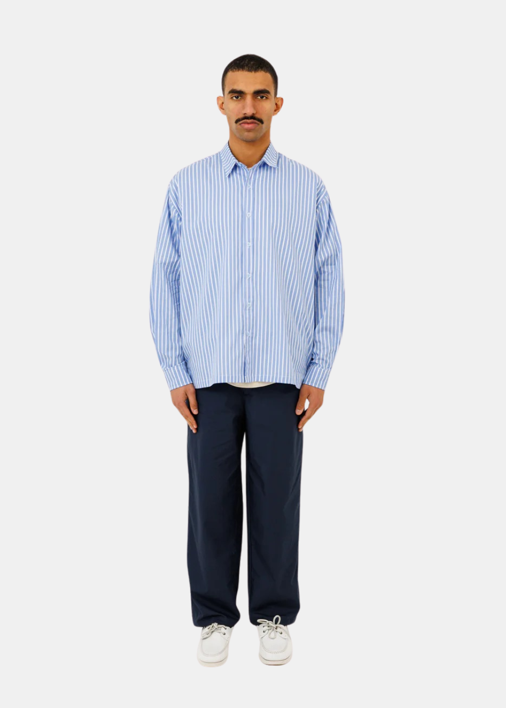 Portrait en pied d'un mannequin portant la chemise rayée bleu et blanc Last Call For Seseh avec un pantalon bleu marine