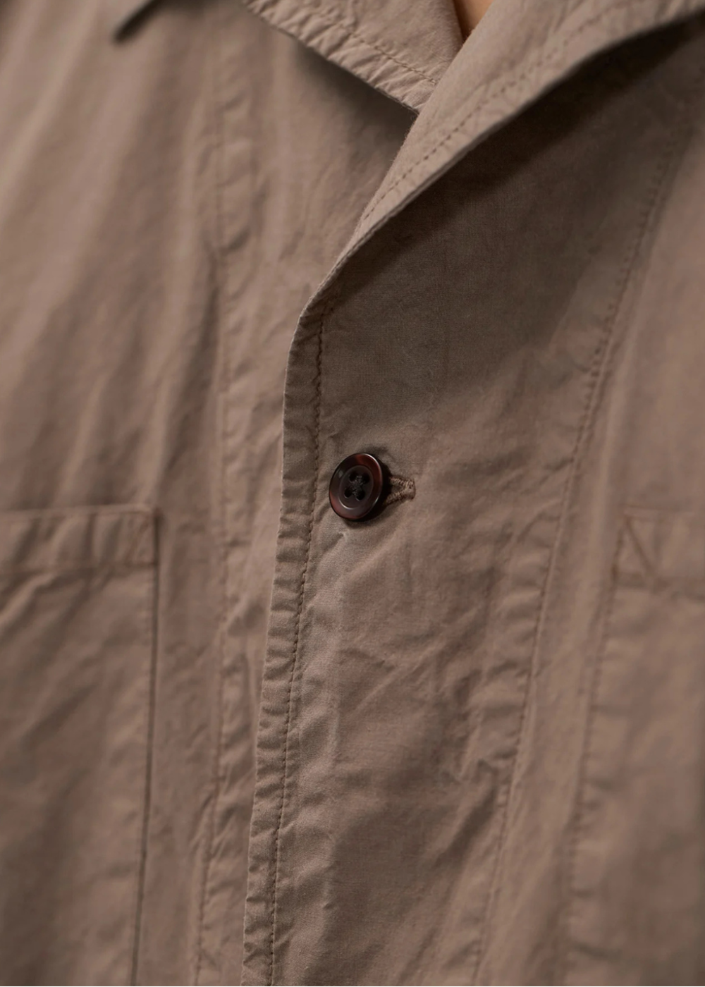 Zoom sur la texture du tissu en Tencel taupe et un bouton brun de la chemise Homme Norse Projects.