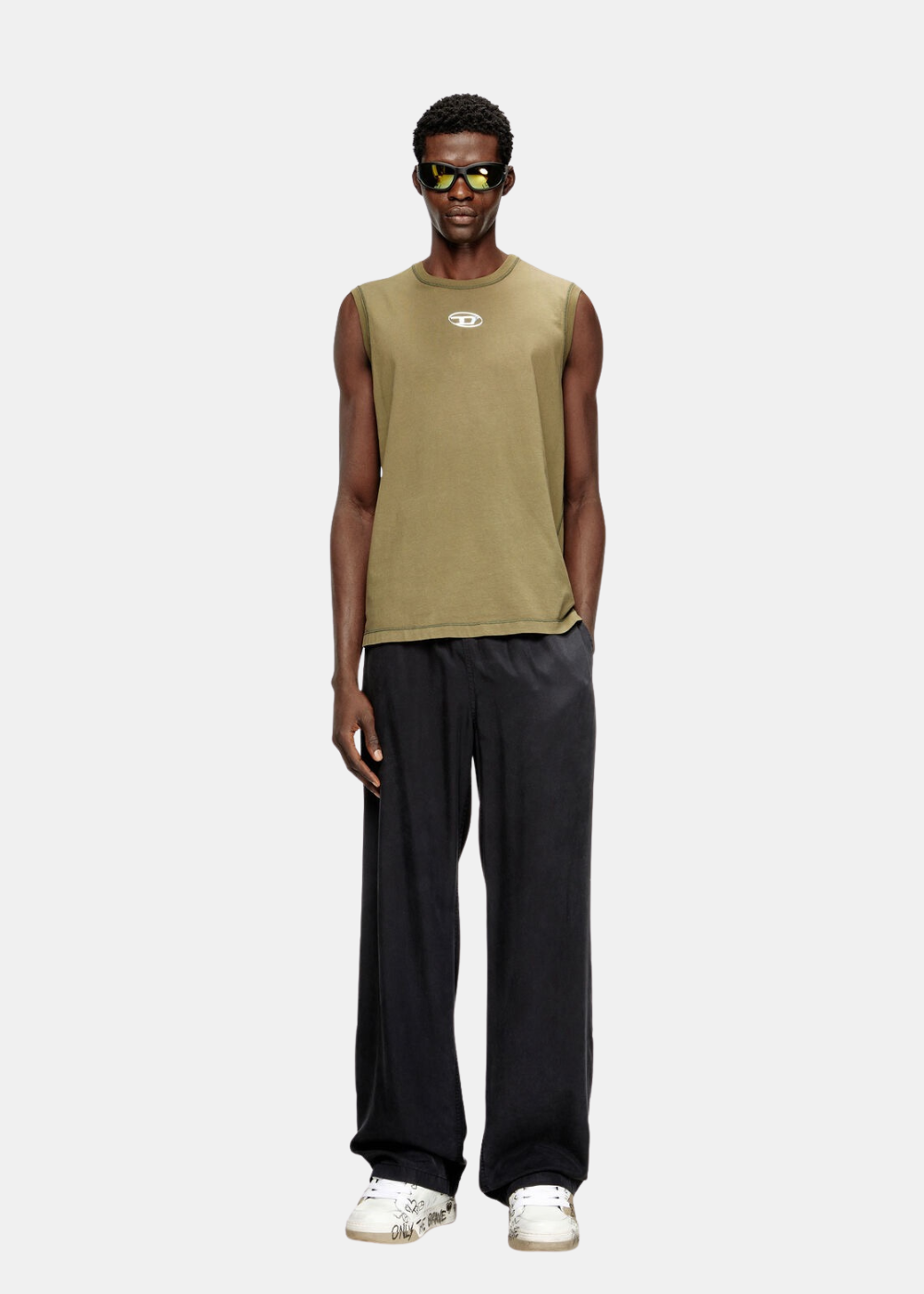 Mannequin homme portant un débardeur vert Diesel avec logo Oval D métallisé, pantalon noir large et baskets blanches.