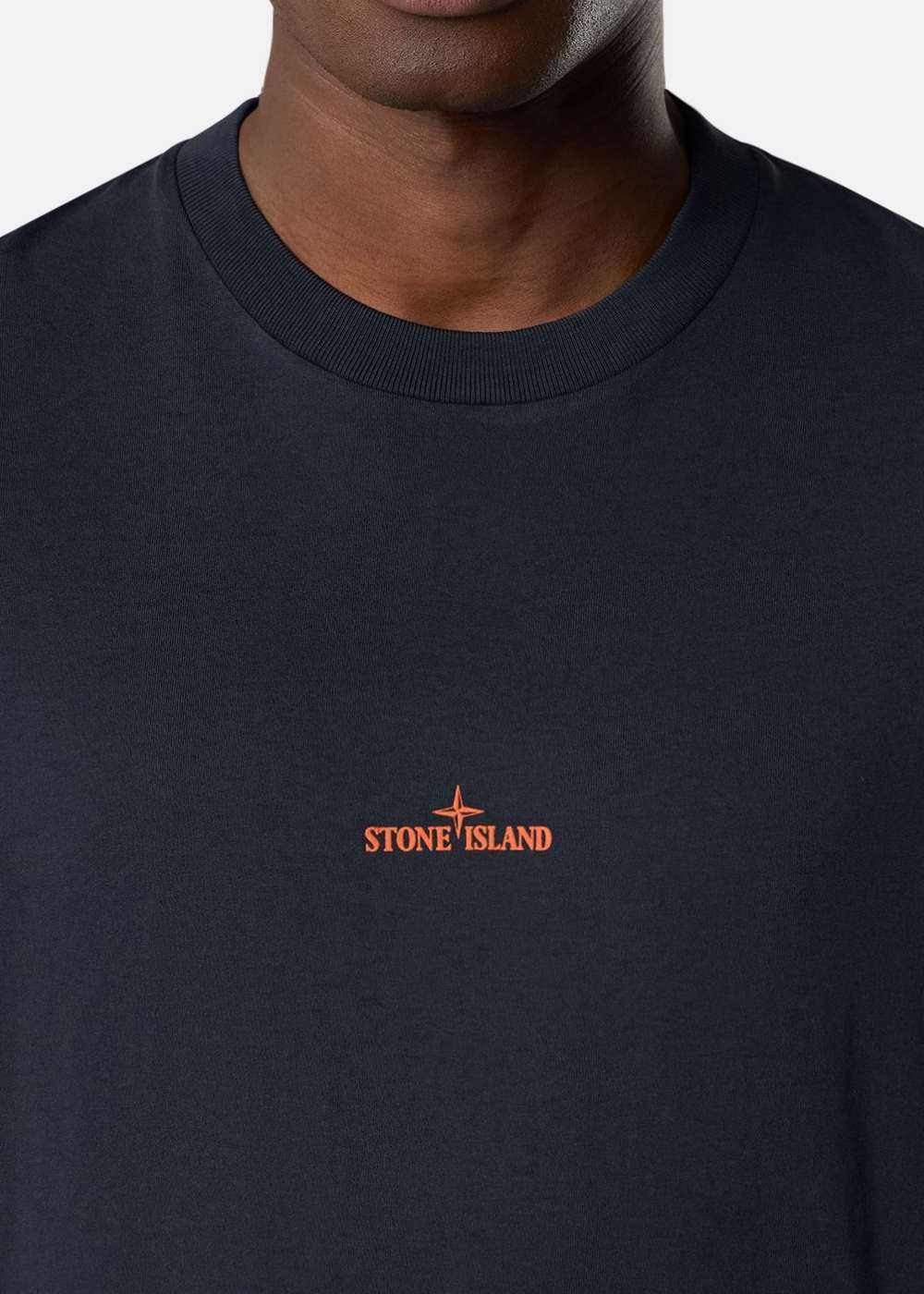 Gros plan sur le col rond et la poitrine du t-shirt marine, mettant en valeur le petit imprimé orange de la marque Stone Island.