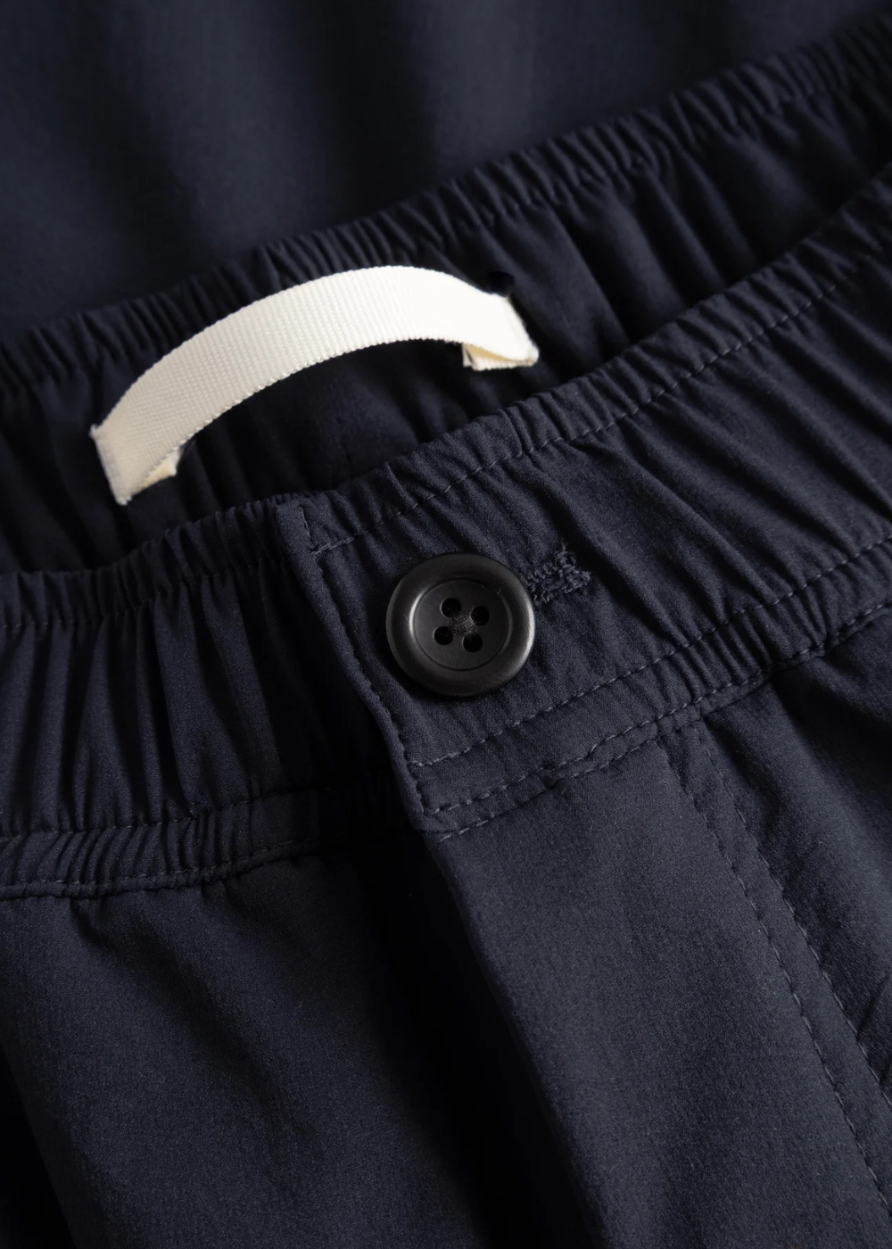 Gros plan sur la matière technique déperlante et les finitions du pantalon bleu marine Norse Projects.