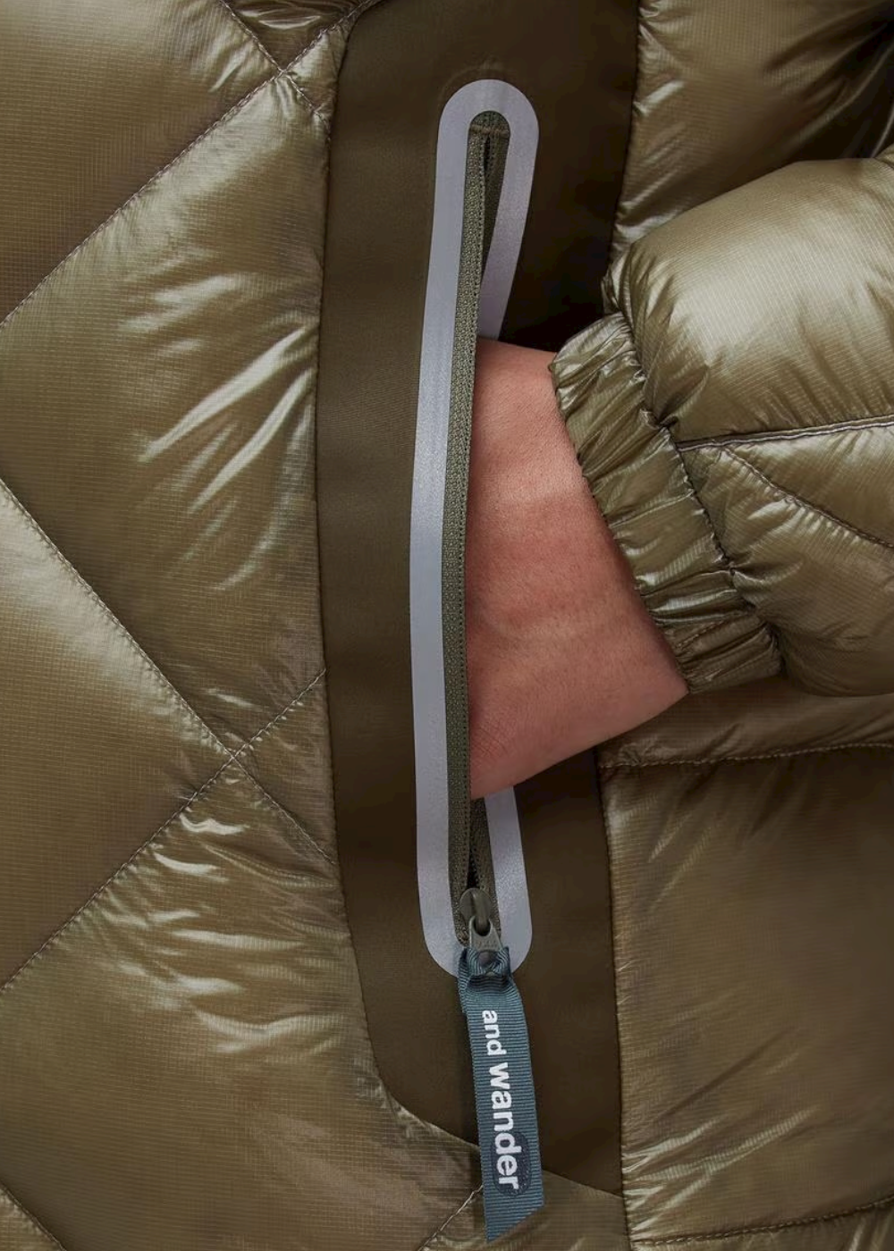 Gros plan sur la poche latérale zippée, le passepoil réfléchissant et le logo And Wander.