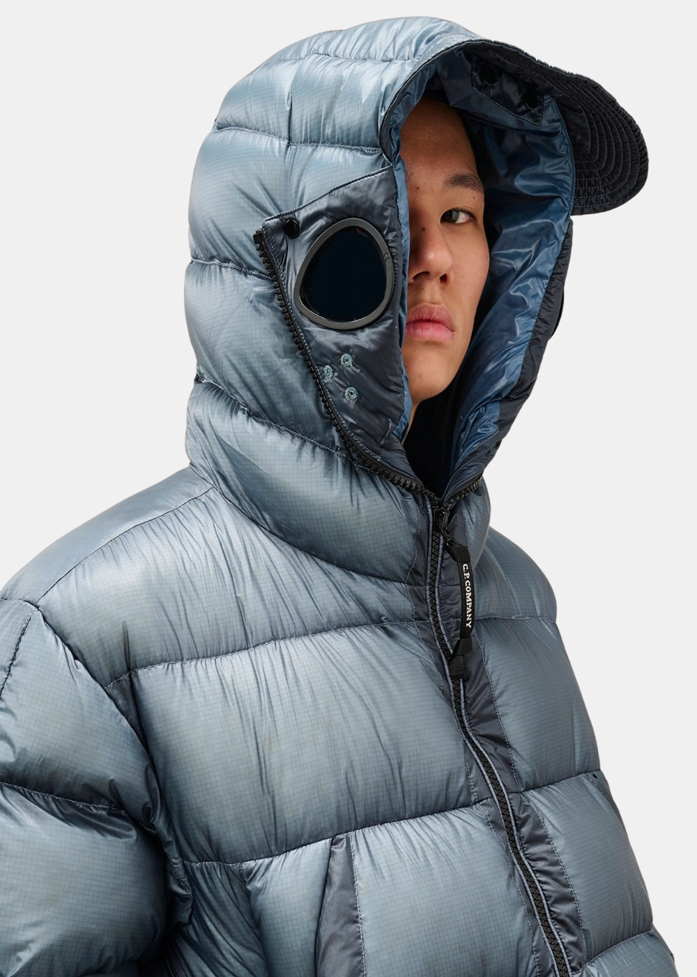 Gros plan porté sur la capuche doudoune C.P. Company Explorer bleue équipée d'une visière et de la lunette intégrée