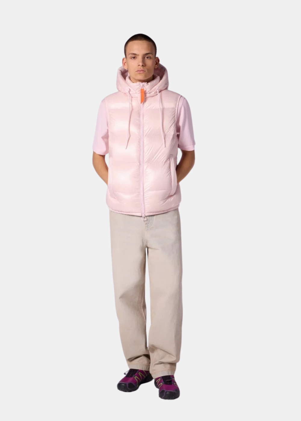 Homme portant la doudoune sans manches Gertrude Cesar rose glossy avec un pantalon beige et des baskets colorées.