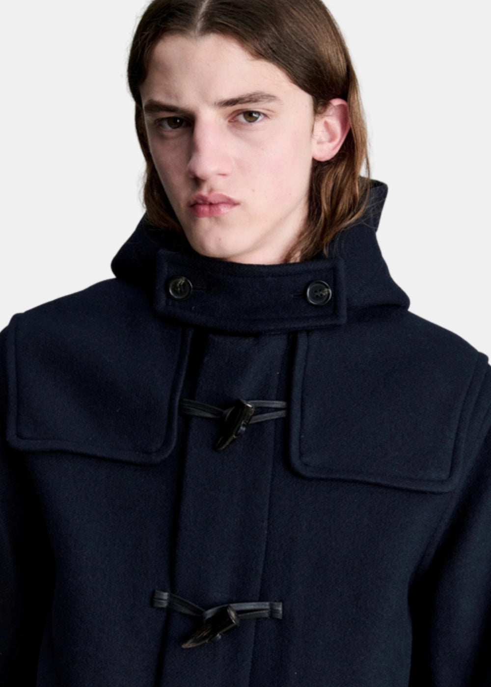 Porté au buste d'un duffle coat A.P.C. Luis marine, avec col montant, capuche et brandebourgs en cuir sur boutons bois.