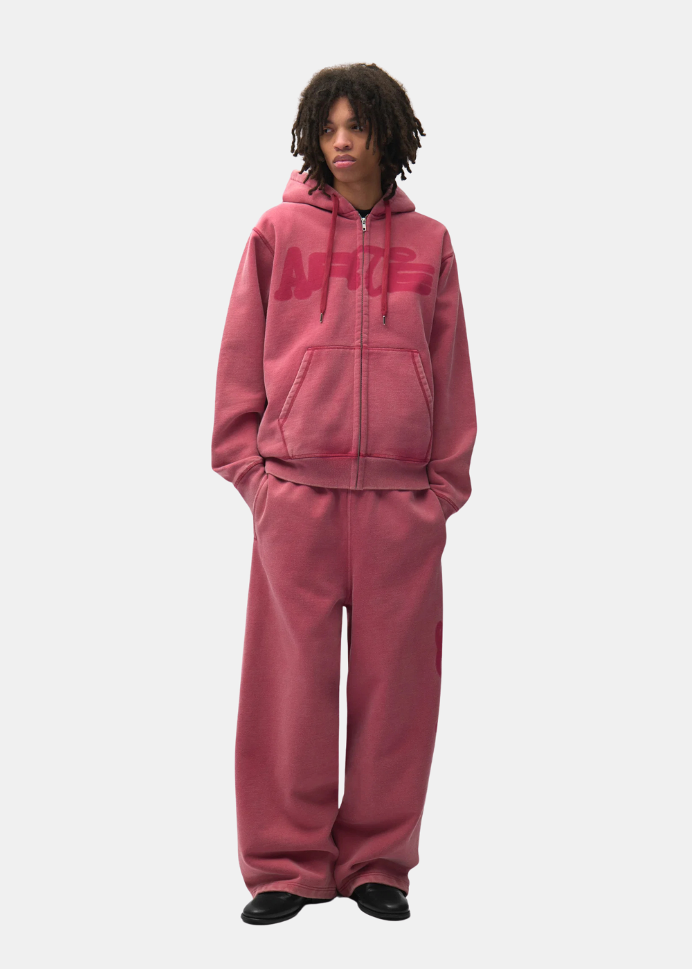Mannequin homme portant le total look tracksuit rouge délavé Arte Antwerp avec sweat à capuche et jogging ample.