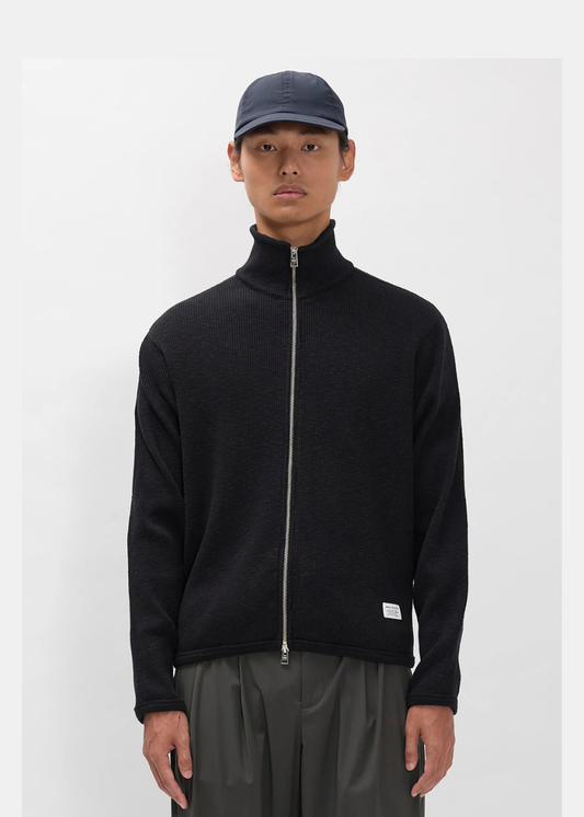 Porté du gilet Homme Norse Projects noir sur un mannequin avec casquette et pantalon gris.