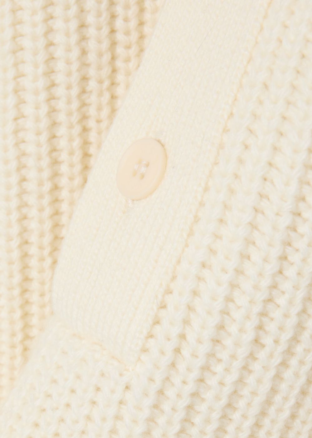 Gros plan sur la maille perlée épaisse en laine et le bouton ton sur ton du pull Lacoste écru.