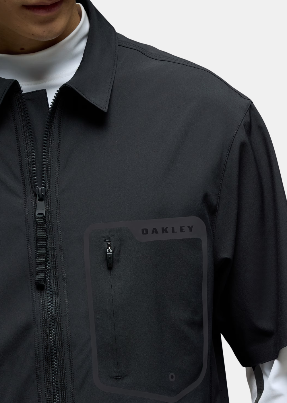 Zoom sur la poitrine de la chemise Oakley noire montrant la poche zippée et le logo Oakley.