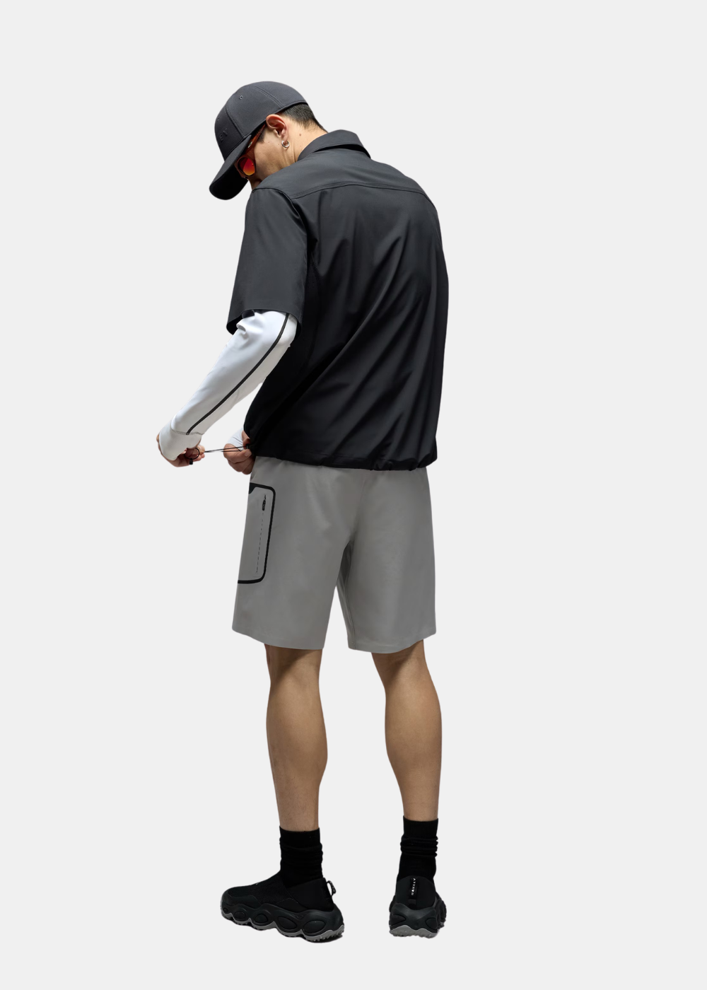 Porté dos d'un look complet avec chemise zippée Oakley noire, short gris et casquette.