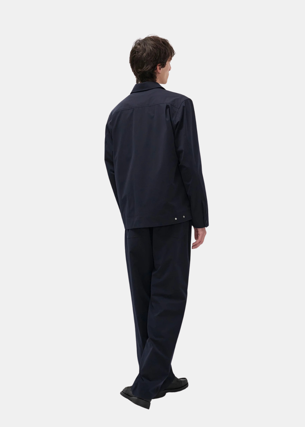 Vue de dos du look complet, un homme porte l'ensemble technique bleu marine Norse Projects.
